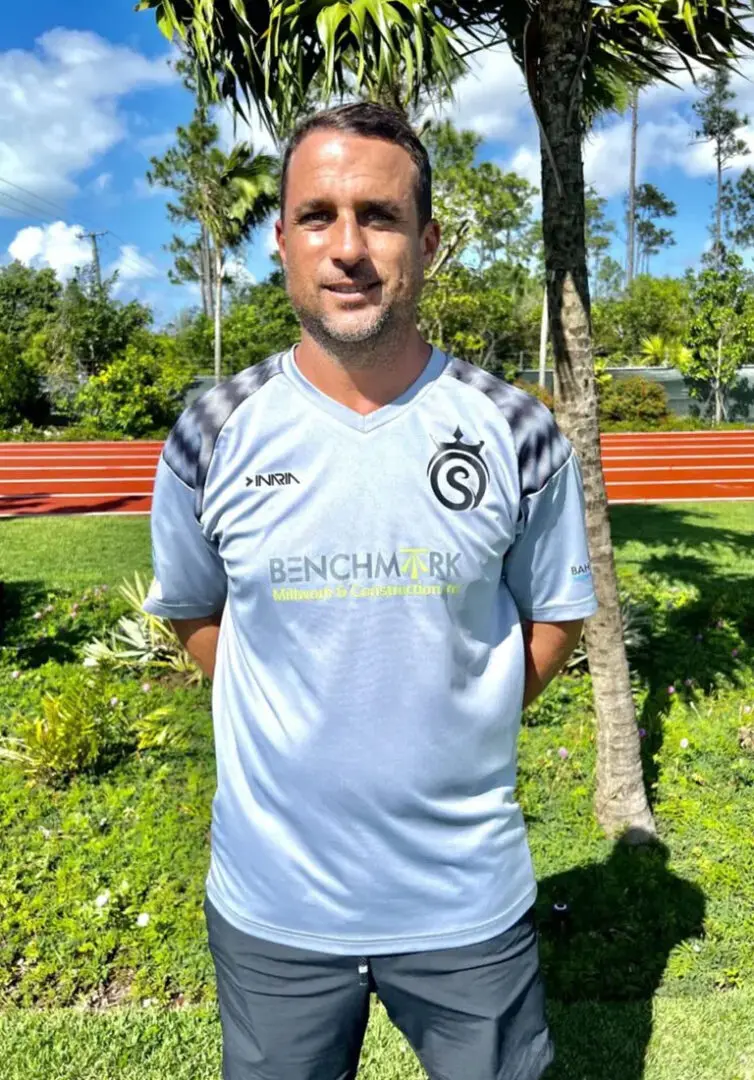 A man in a soccer uniform standing next to a tree.